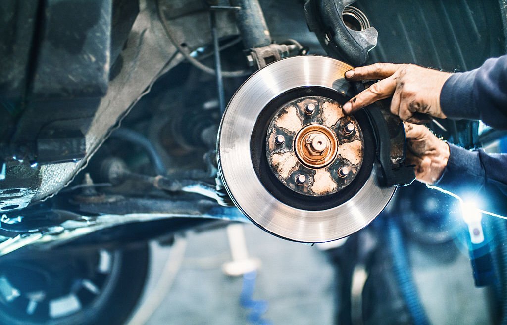Closeup of unrecognizable male mechanical replacing worn out brake pads on a vehicle. The wheel has been removed and the car is lifted up on a jack. Visible braking disc. Side view.